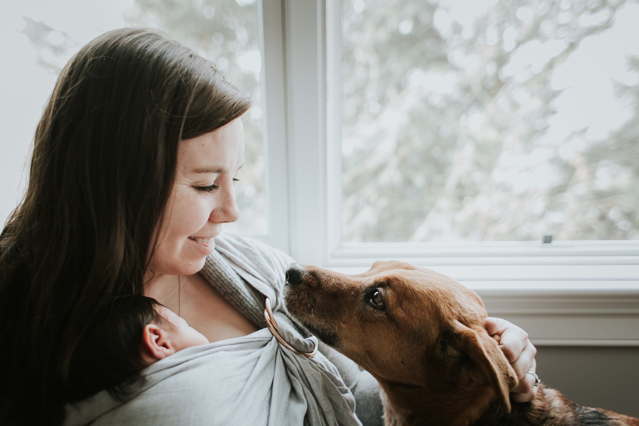 Mother wearing newborn ring sling and petting dog. 