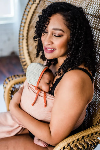 Mother holding her baby in a ring sling sitting on a chair.