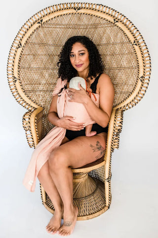 Mother holding her child in a ring sling. She is sitting in a peacock chair.