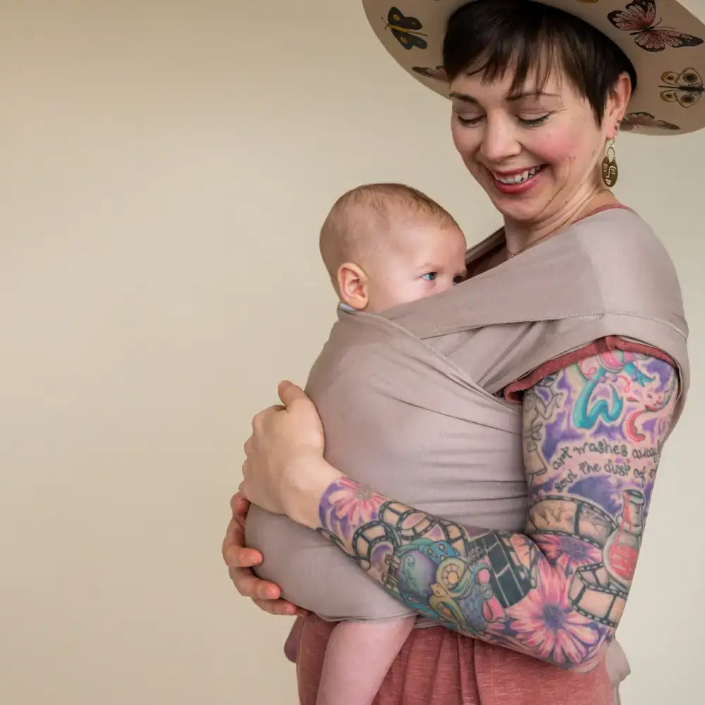 Mother smiling and wearing baby in tan stretchy baby wrap carrier