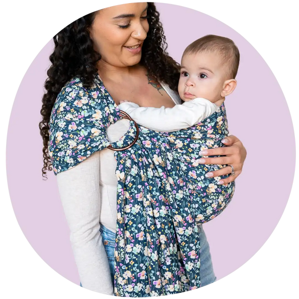 A Black mother smiling at her baby in a baby floral ring sling baby carrier. 