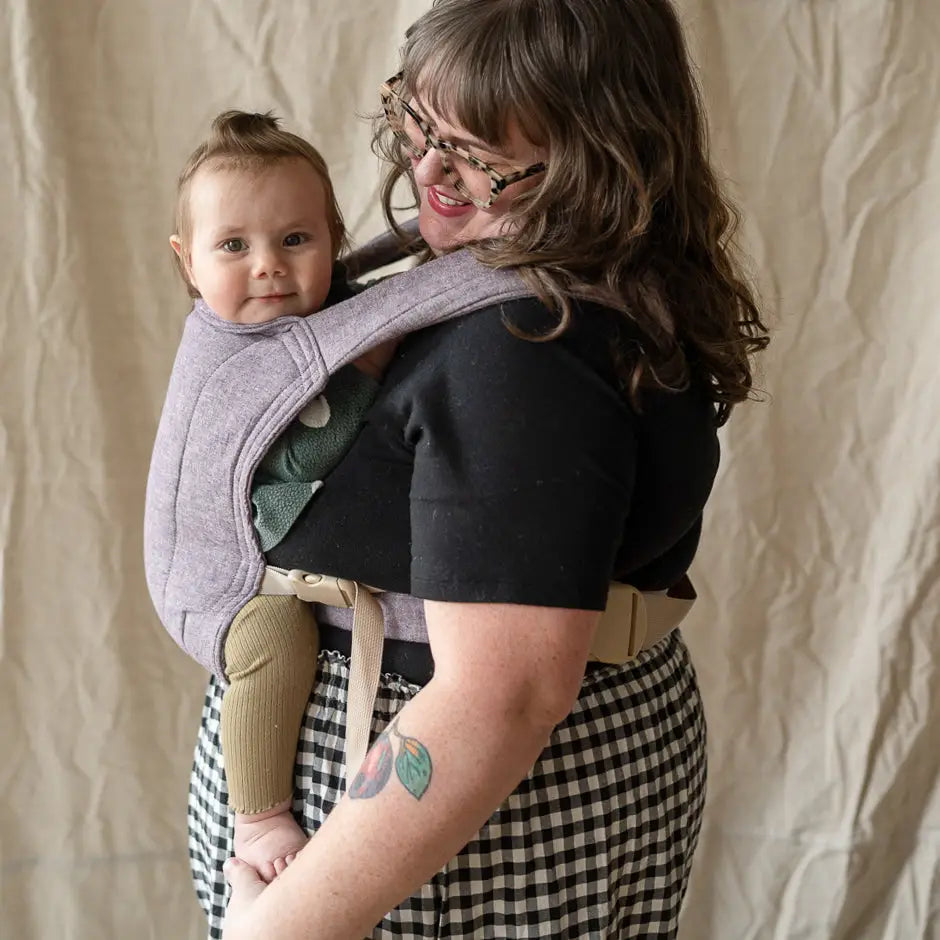 Plus size woman smiling and wearing a baby in a purple lark baby carrier. 