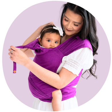 An Asian mother smiling and babywearing her toddler in a purple meh dai carrier 