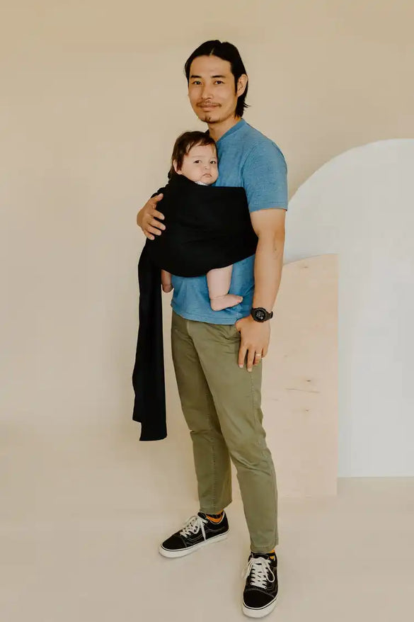 Asian father holding his baby in a black ring sling baby carrier. 