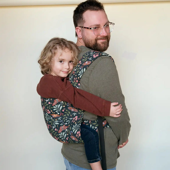 Man carrying child in floral baby carrier.