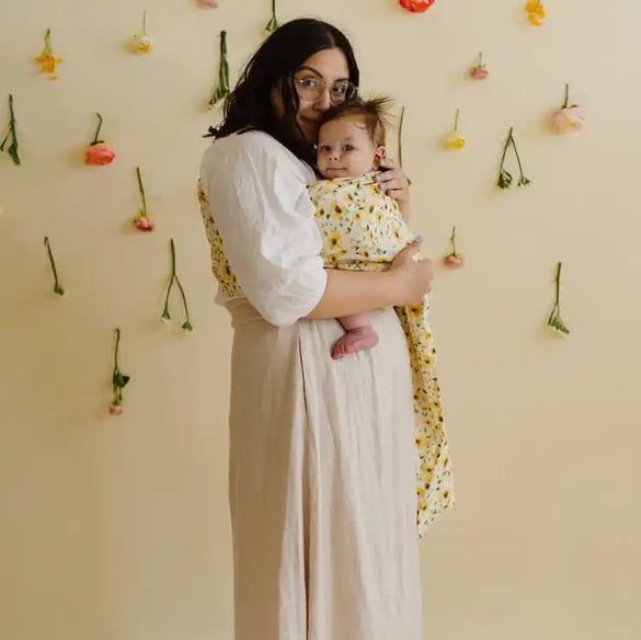 Mother holding baby in floral wrap.