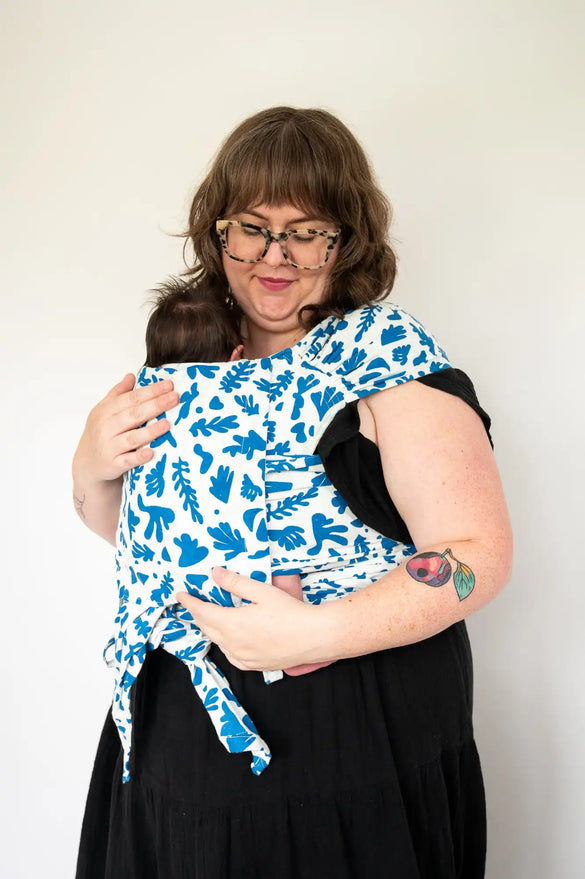 Woman holding baby in patterned carrier.